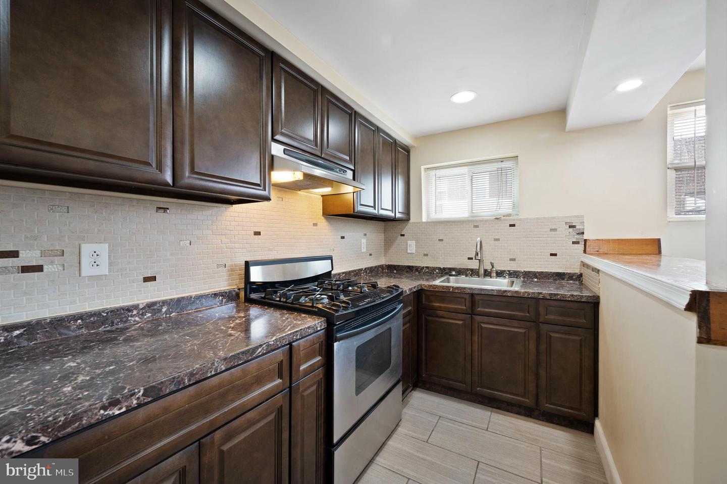 Kitchen with dark wood cabinets, stone countertops, gas range, and light tile backsplash.