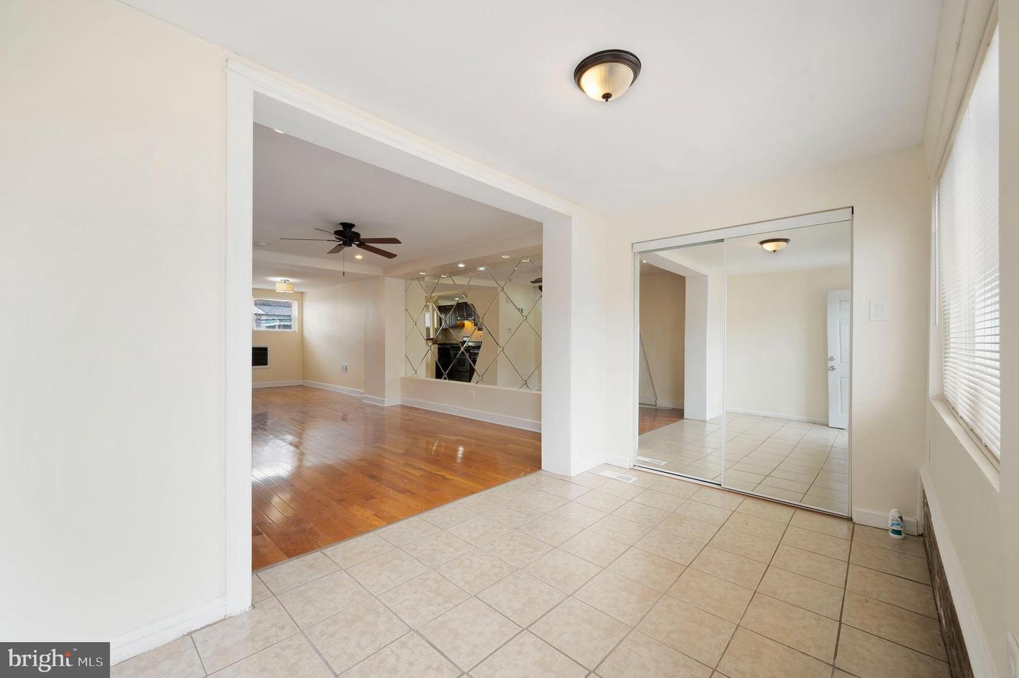 Tiled interior area opening to a hardwood-floored living room with a mirrored accent wall.