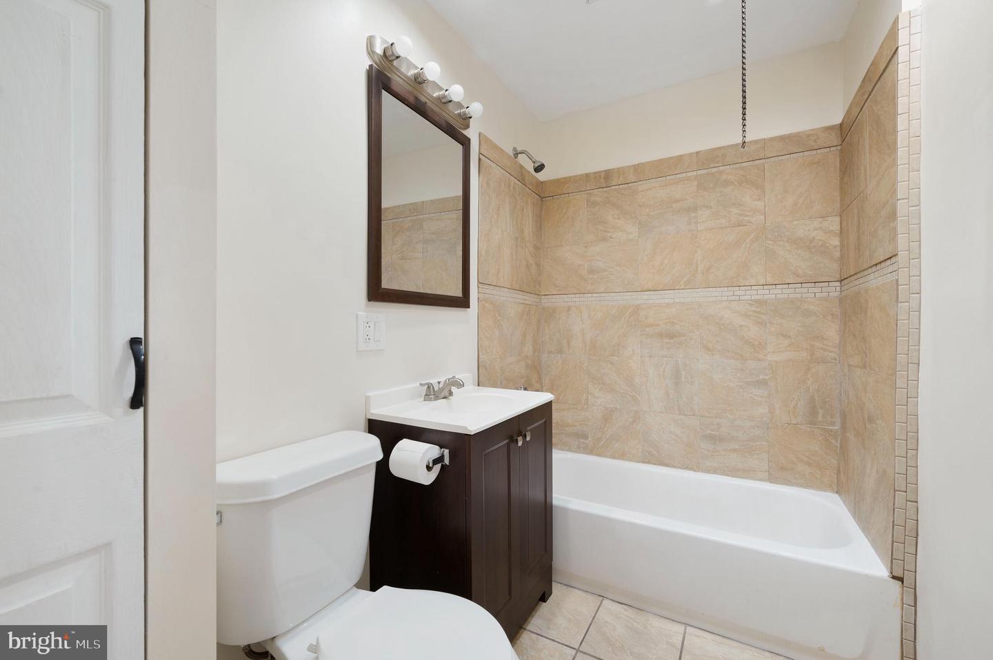 Bathroom with a beige tiled tub surround, white bathtub, toilet, and dark wood vanity.