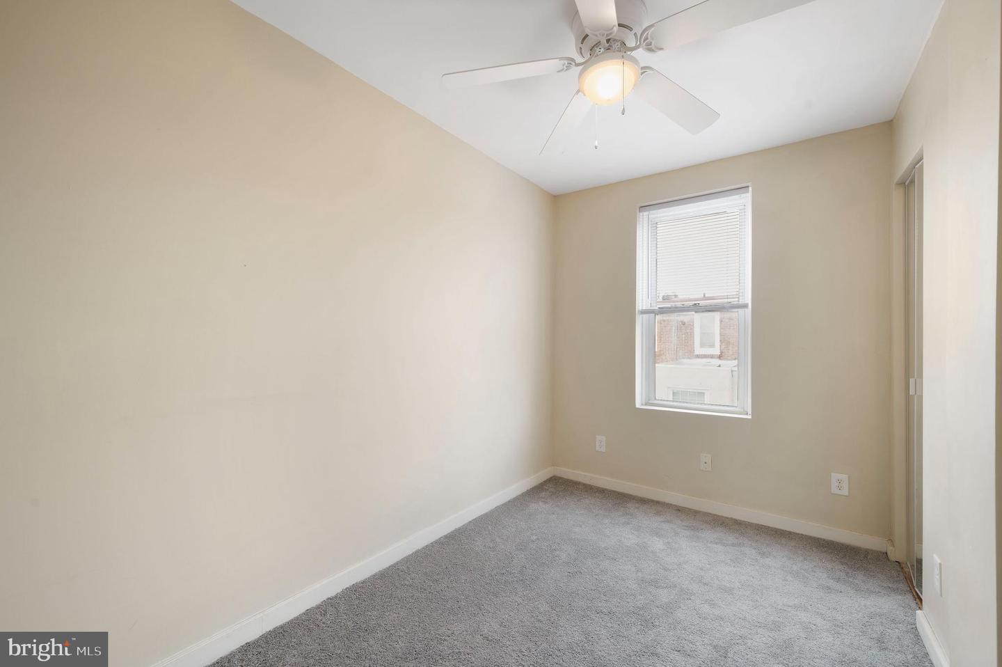 Empty bedroom with gray carpet, a window with blinds, and a ceiling fan.