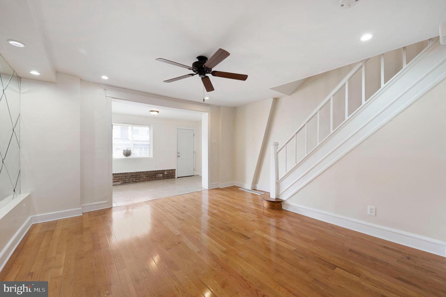 Living room with hardwood floors, a ceiling fan, and an open view into a tiled room.