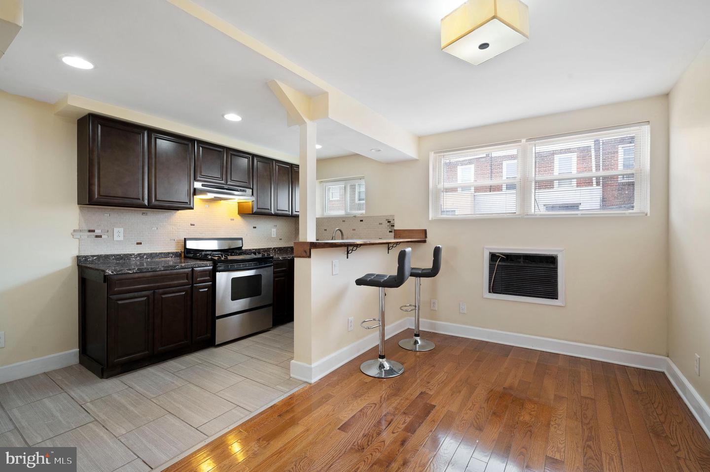 Open kitchen and dining area with dark cabinets, stainless-steel range, breakfast counter, and hardwood floors.
