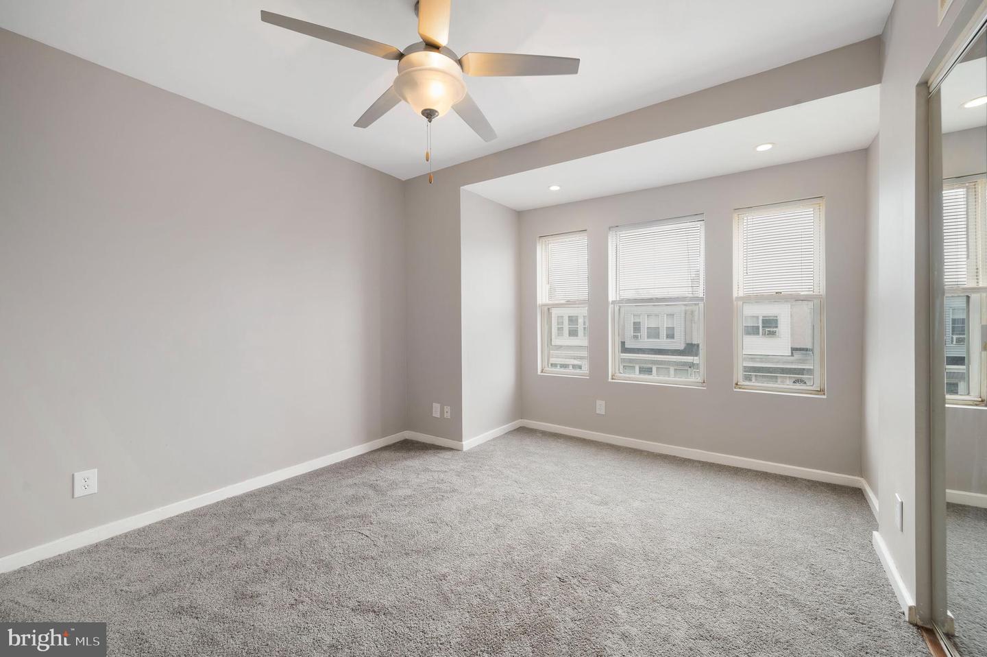 Empty bedroom with gray carpet, a ceiling fan, and three windows with blinds.