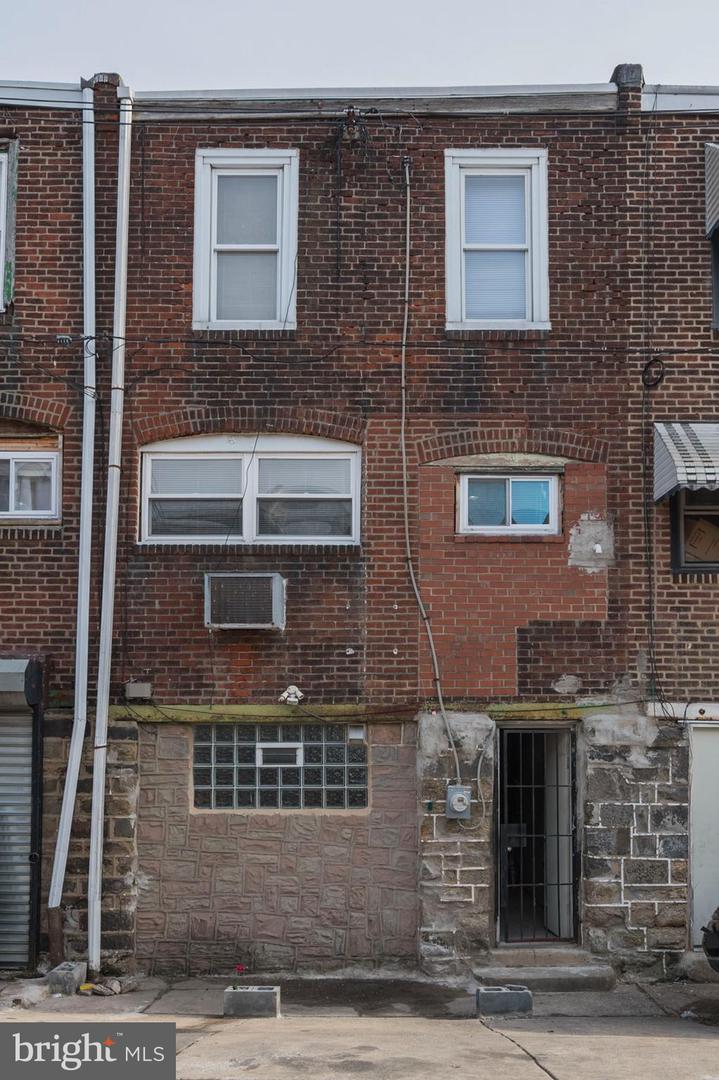 Brick rowhouse facade with white-trimmed windows, a barred entrance, and glass-block basement windows.
