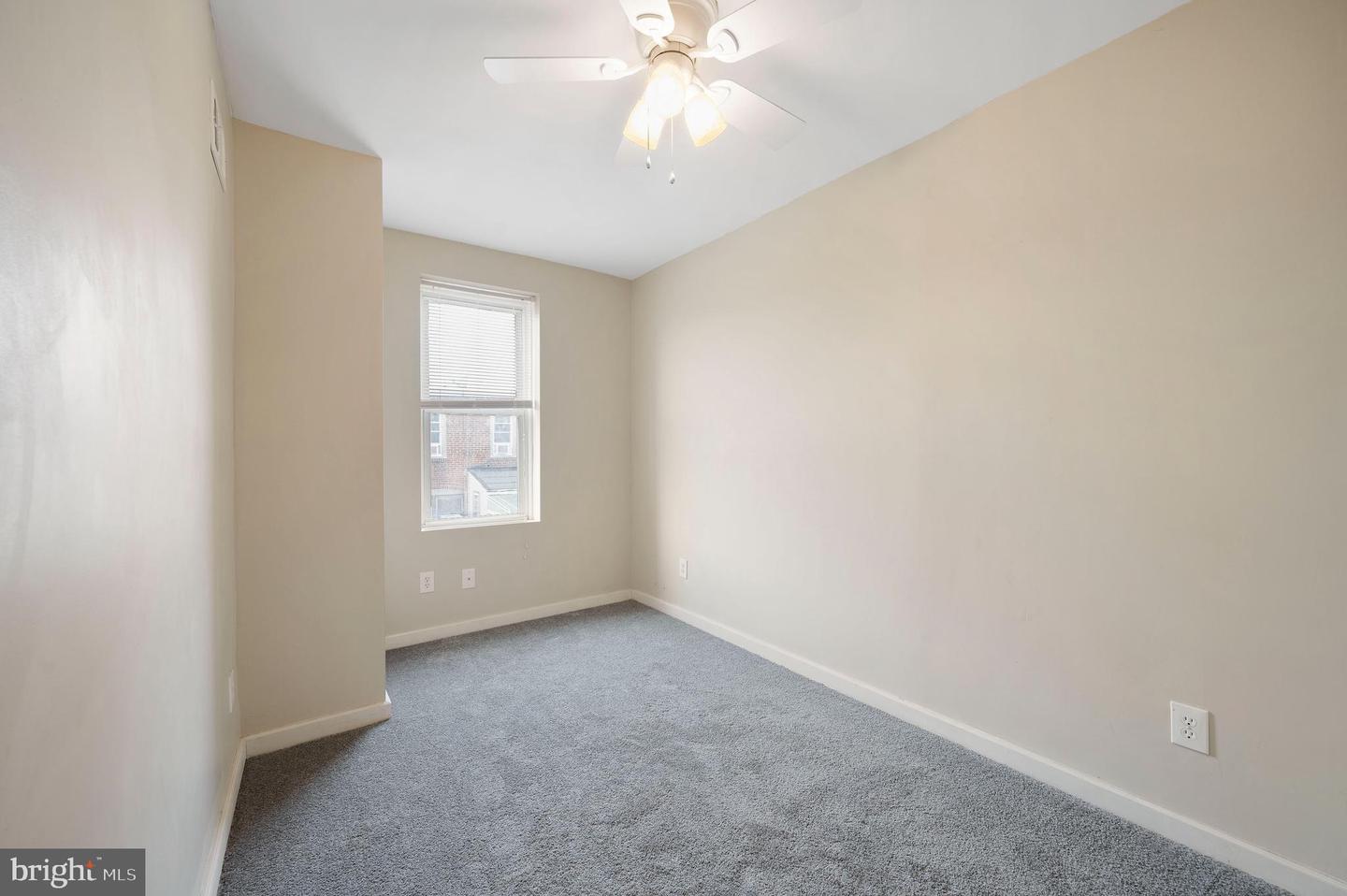 Empty bedroom with gray carpet, a window with blinds, and a ceiling fan with lights.