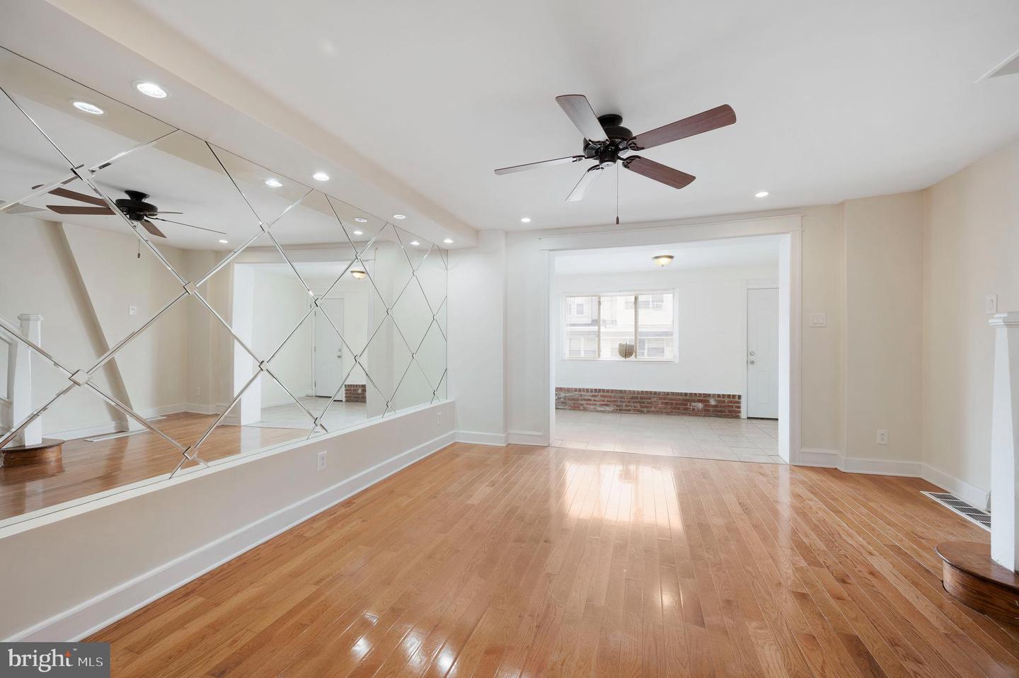 Empty living room with mirrored wall, hardwood floors, and a ceiling fan.