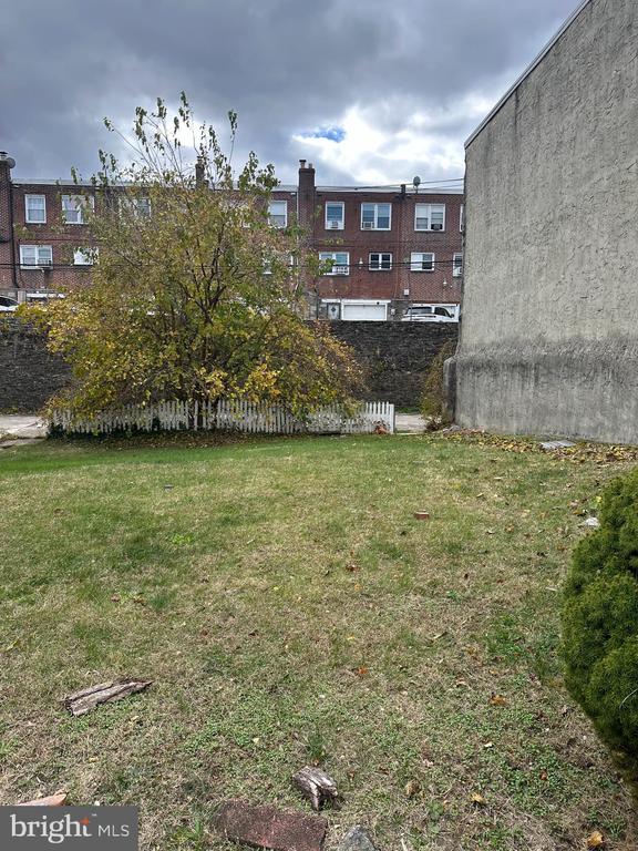 Grassy rear yard with a mature tree, short white fence, and neighboring brick rowhouses.