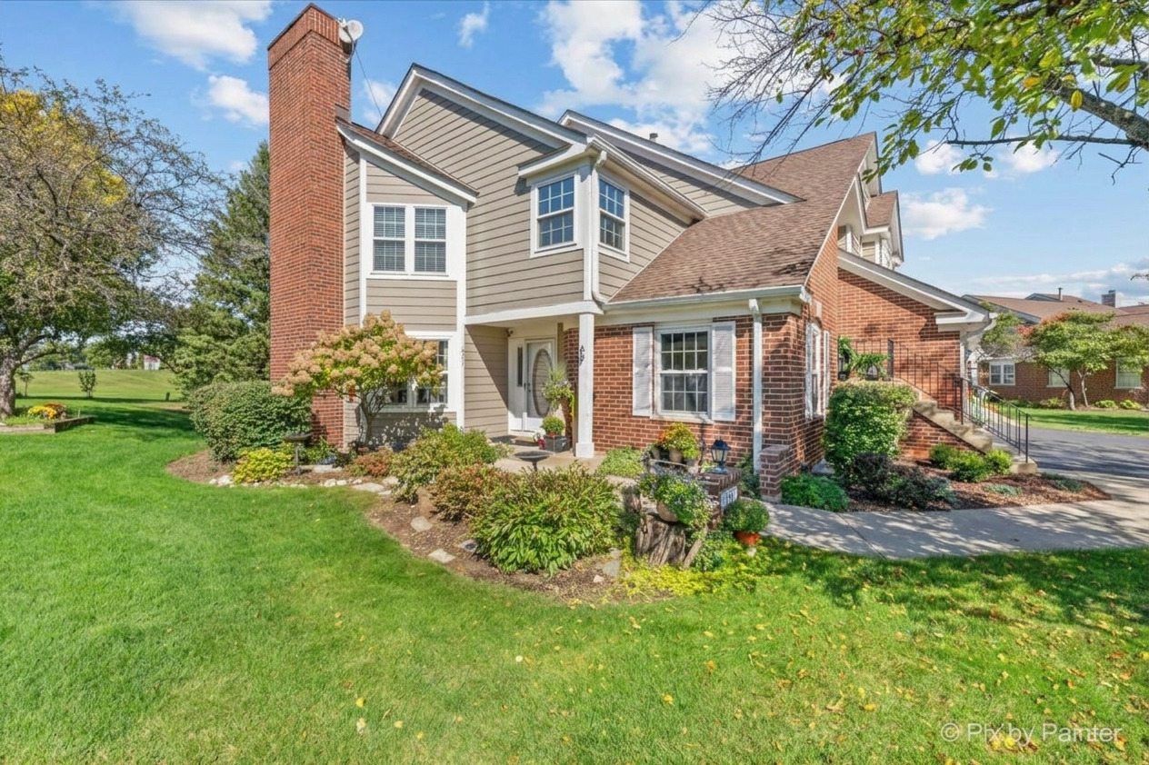 Two-story home with beige siding, brick accents, a tall chimney, and landscaped lawn.