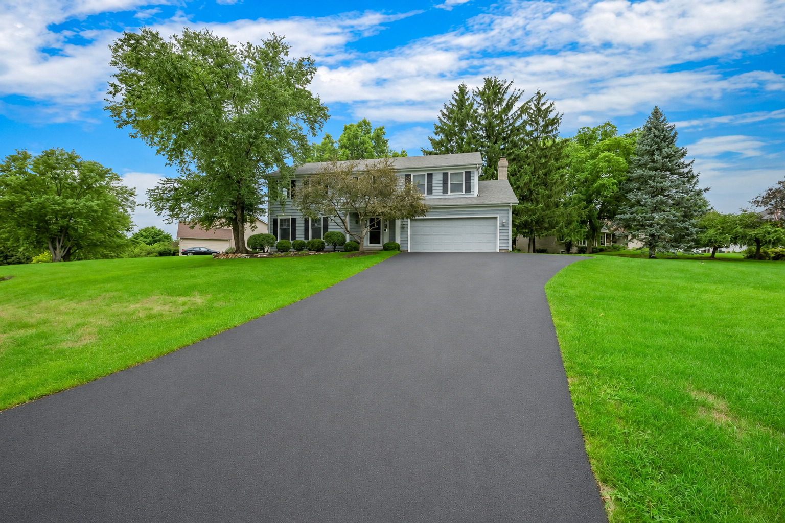 Two-story suburban home with an attached garage, broad driveway, and mature trees.