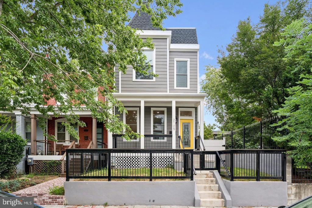 Two-story gray home with a yellow front door, raised front yard, and black metal fence.
