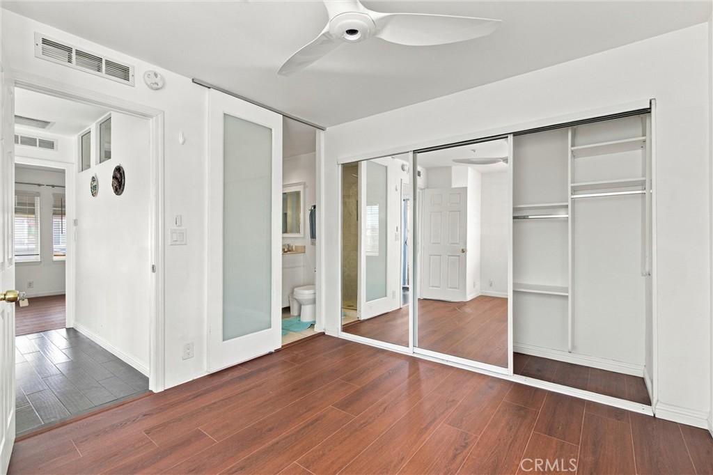 Empty bedroom with mirrored closet doors, wood flooring, and an adjoining bathroom.