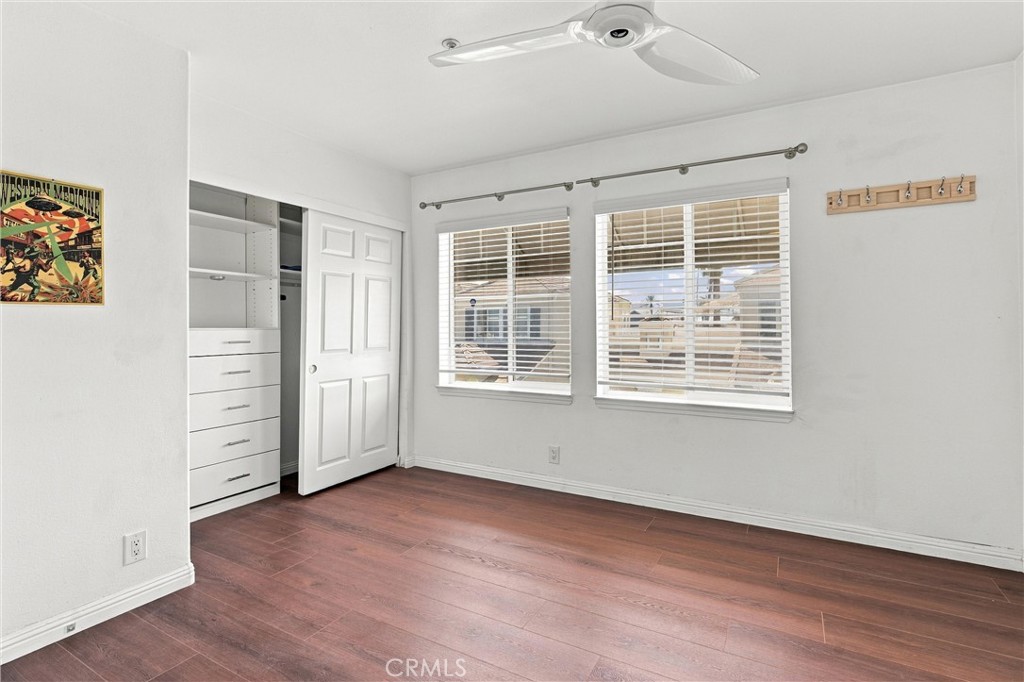 Empty bedroom with built-in closet shelving, reddish-brown floors, and marina views through two windows.