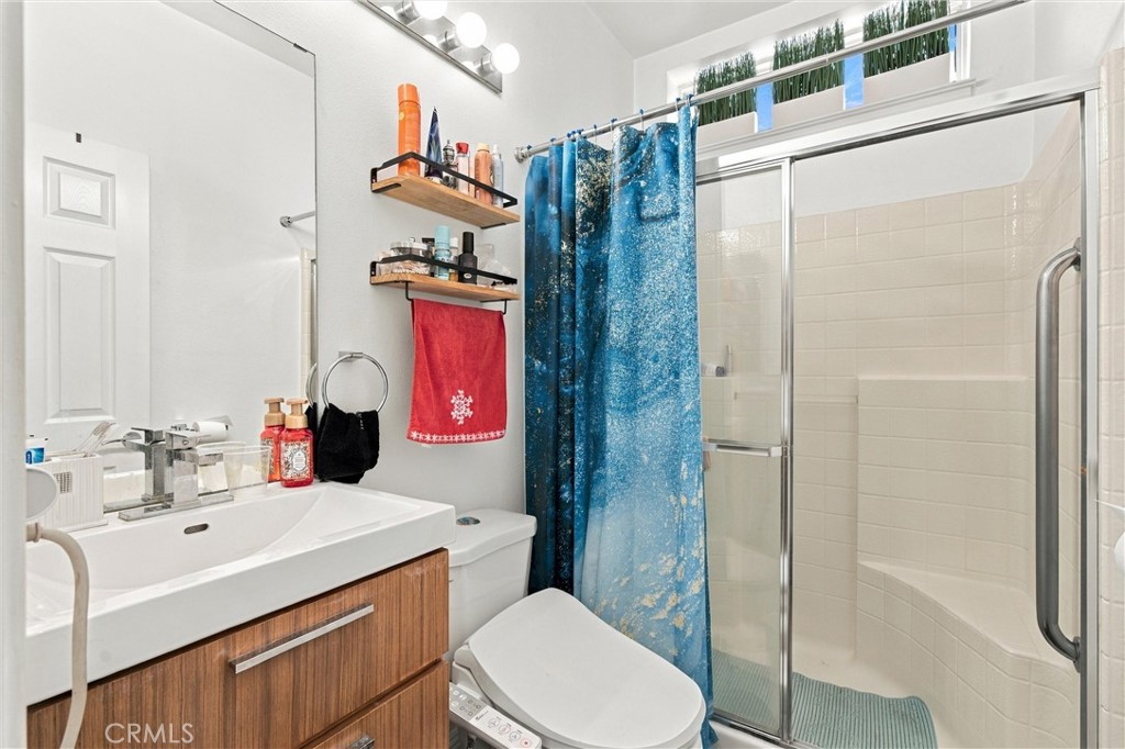 Bathroom with a wood-front vanity, toilet, and glass-enclosed shower with a blue patterned curtain.