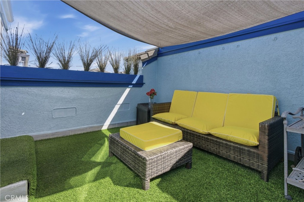 Patio with yellow-cushioned wicker seating on artificial turf beneath a shade canopy.