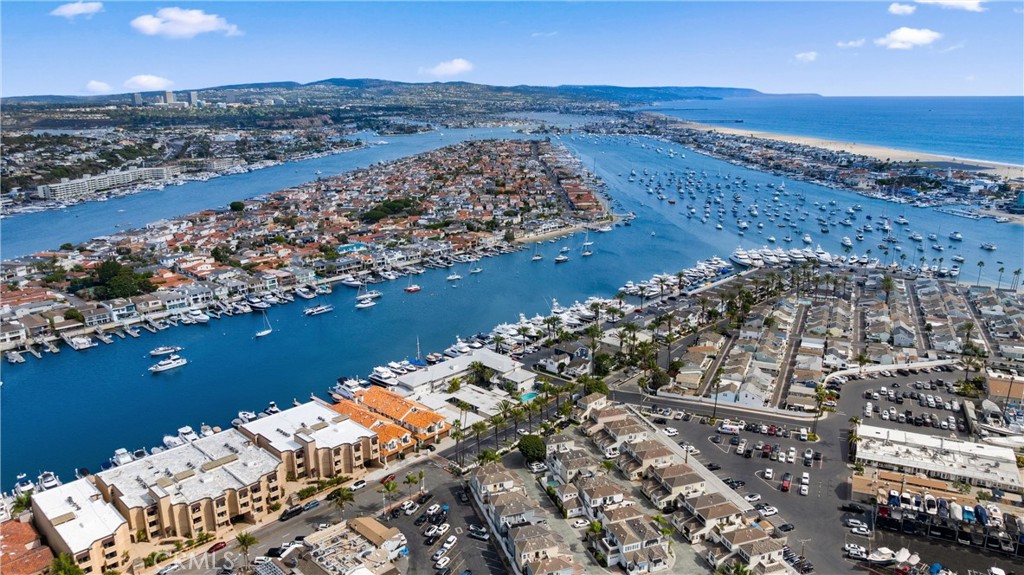 Aerial view of Newport Harbor, with boats moored between waterfront homes and the Pacific Ocean beyond.