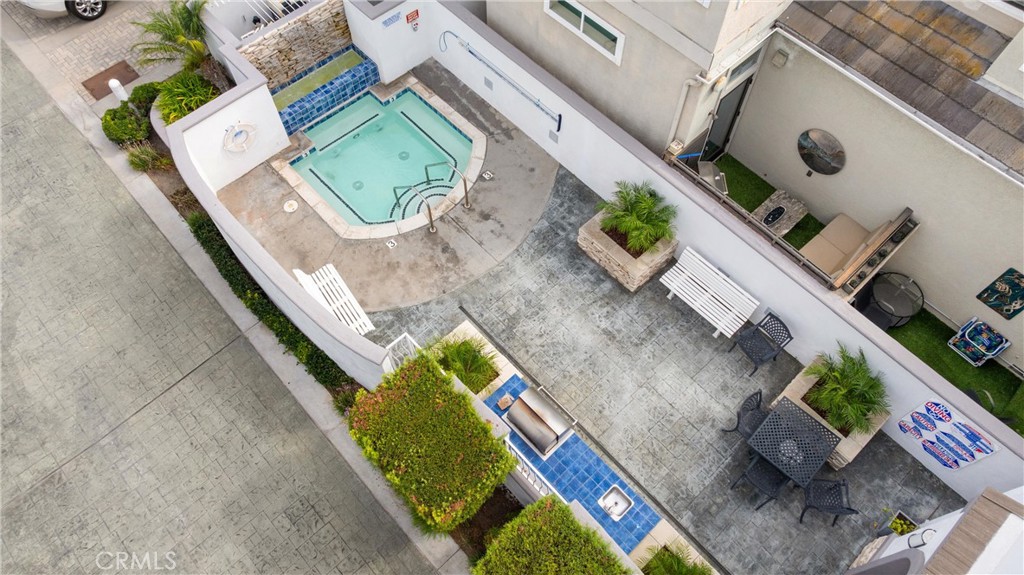 Aerial view of a courtyard pool and spa surrounded by paved patio, lounge chairs, and planters.