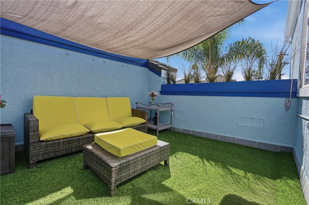 Outdoor patio with yellow-cushioned wicker seating, artificial grass, and a fabric shade canopy.