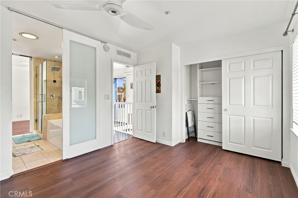 Vacant bedroom with wood flooring, built-in closet, and an adjoining tiled bathroom.