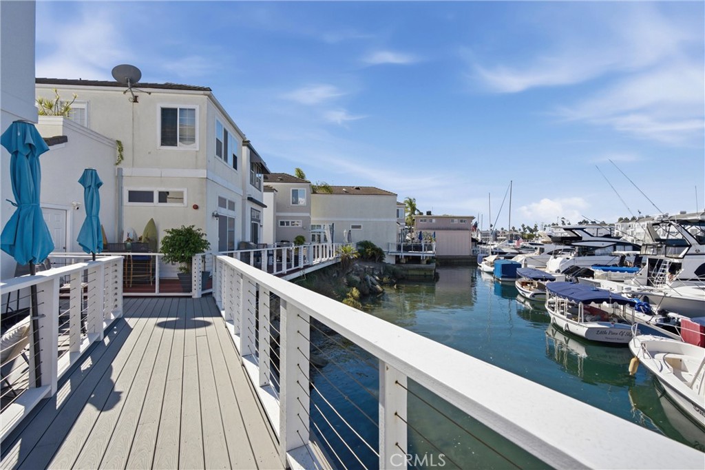 Waterfront walkway beside marina homes, with white railings and boats moored along the harbor.