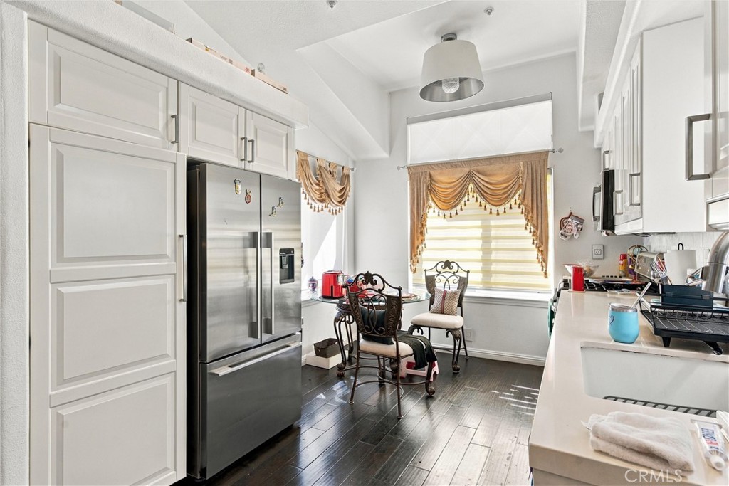 Bright kitchen with white cabinetry, stainless-steel refrigerator, dark floors, and a dining table by the window.