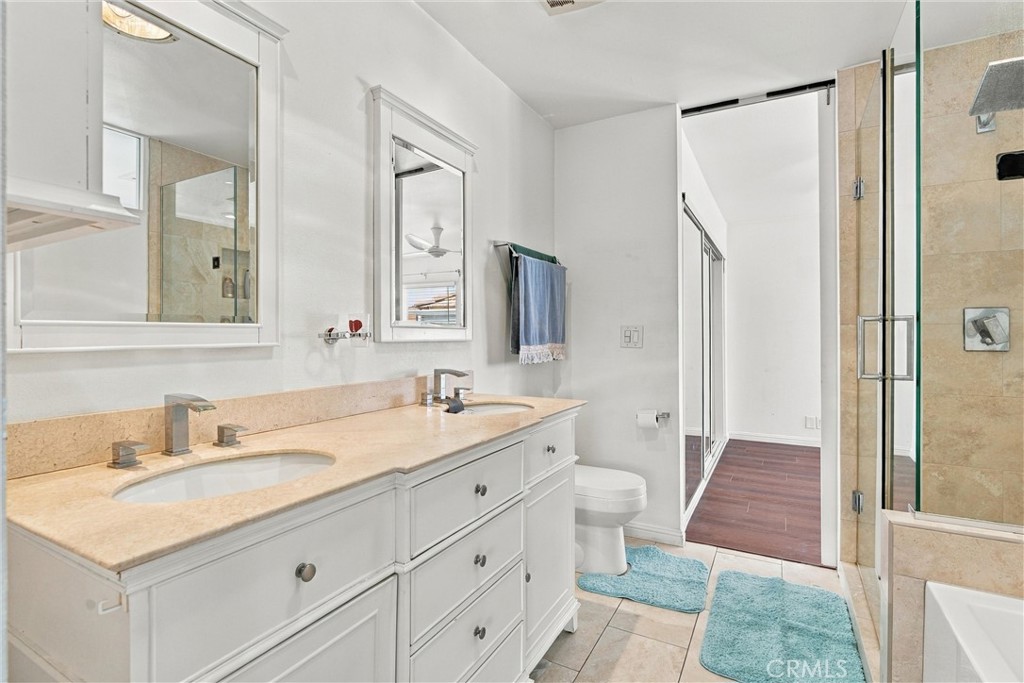 Bathroom with a white double vanity, pale stone countertop, and glass-enclosed shower.