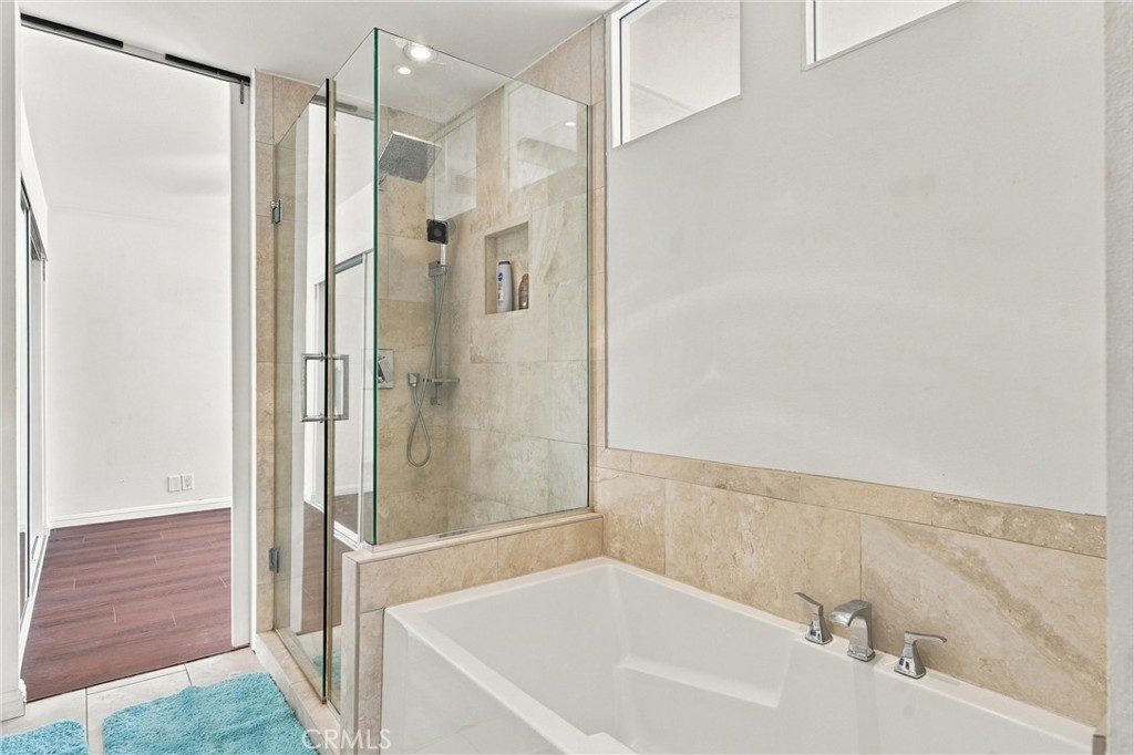 Bathroom with a white soaking tub and glass-enclosed, beige-tiled shower.