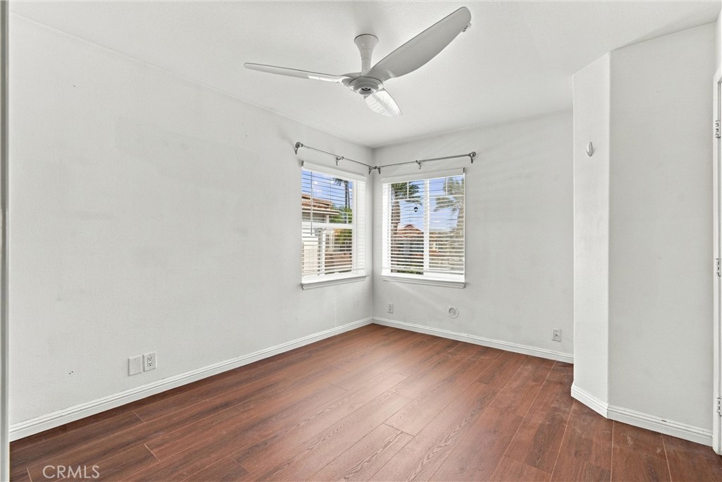 Empty room with wood floors, a ceiling fan, and two windows with blinds.