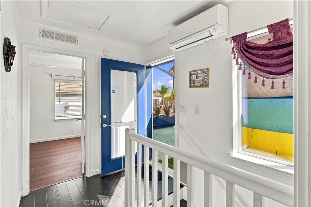 Entry hall with a blue front door, white stair railing, and windows facing a sunny outdoor area.