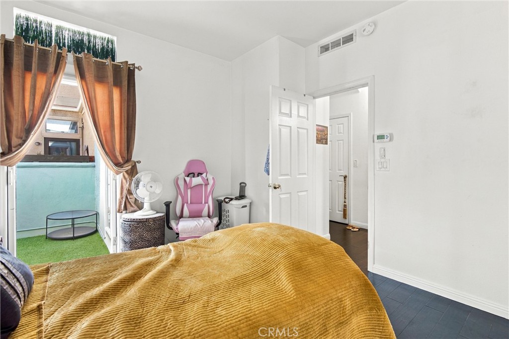 Bedroom with a mustard-yellow bedspread and pink gaming chair beside a glass door to a turf-covered balcony.