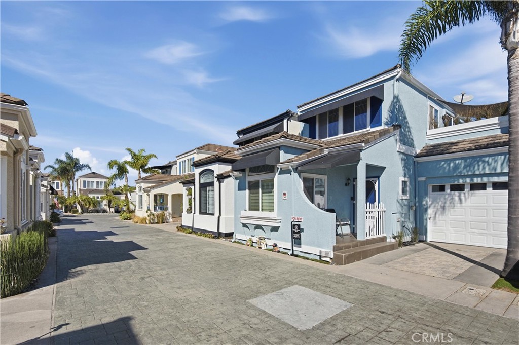 Blue two-story home with a small gated entry and attached garage on a palm-lined residential lane.