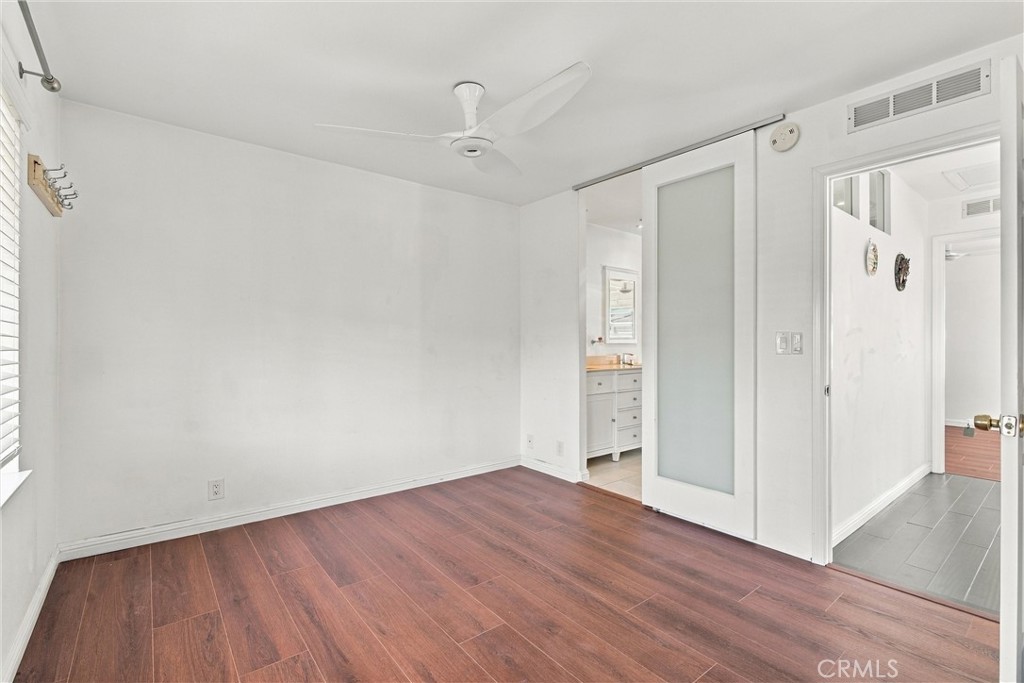 Empty bedroom with reddish-brown flooring, a ceiling fan, and a sliding frosted-glass door.