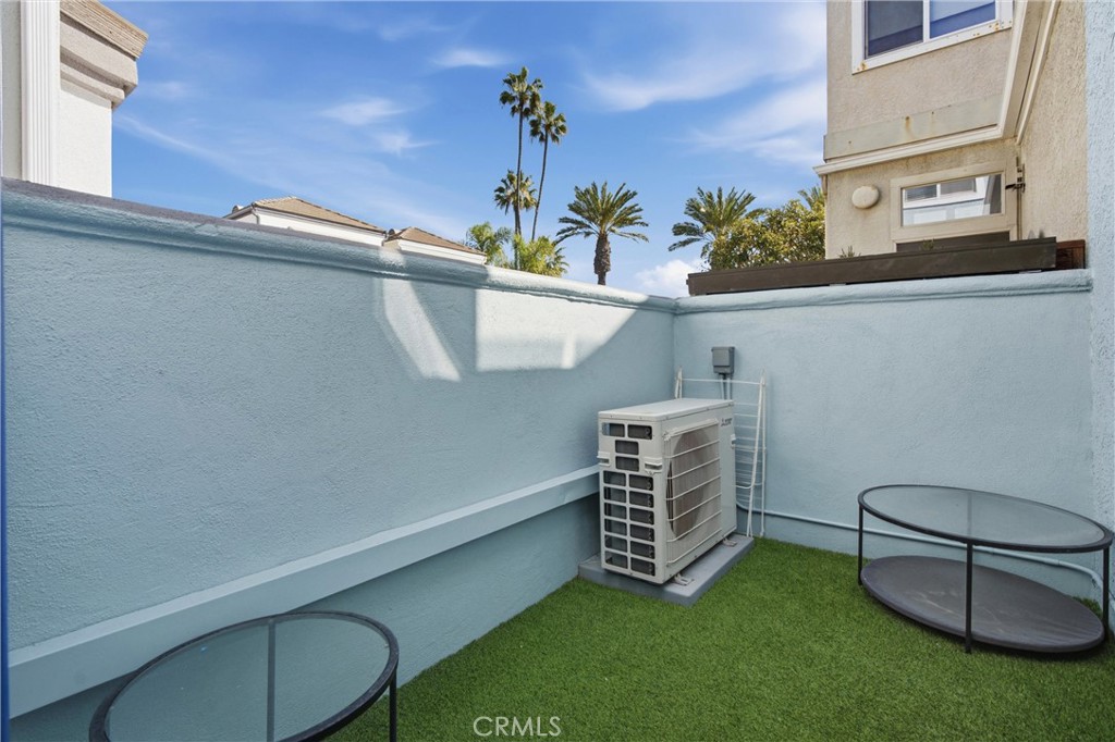 Enclosed patio with artificial grass, glass-top tables, and an outdoor air-conditioning unit.