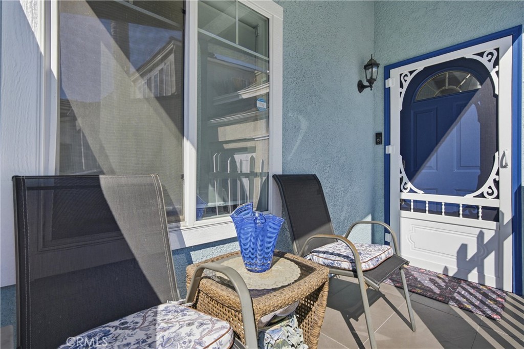 Front porch with cushioned chairs, a wicker table, and a blue door with decorative white trim.