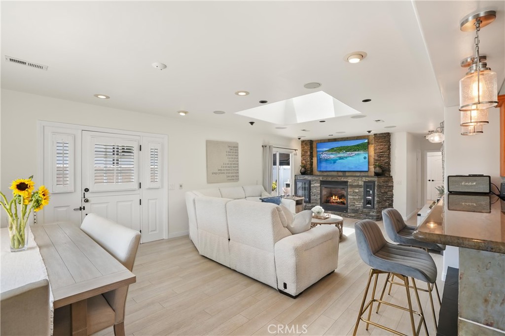 Open living room with a stone fireplace, wall-mounted television, and adjacent kitchen island.