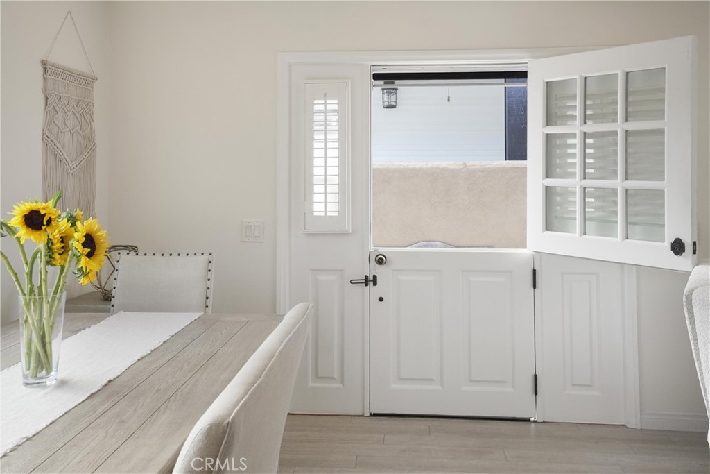 Dining area with a light wood table and sunflowers beside an open white Dutch door.