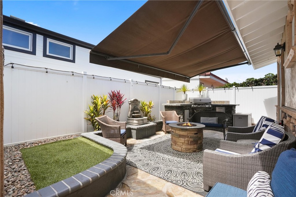 Furnished backyard patio with a stone fire pit, outdoor kitchen, fountain, and retractable shade canopy.