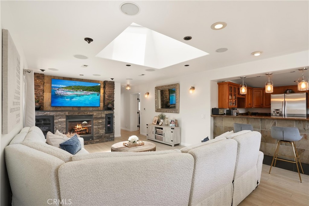 Living room with a stone fireplace, large white sectional, skylight, and open kitchen.