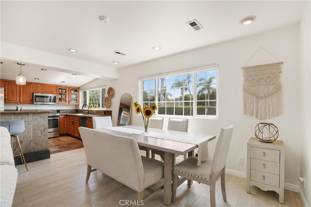 Dining area with a white table and upholstered chairs beside a wood-cabinet kitchen and large windows.