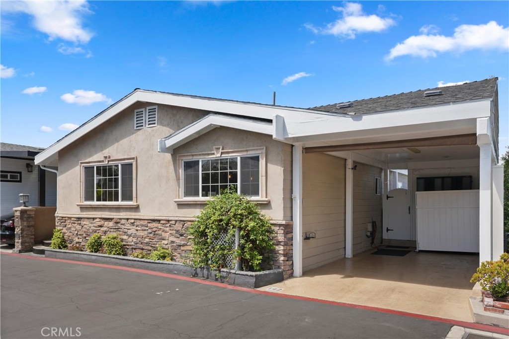 Single-story beige home with stone facade, front windows, and a covered carport.