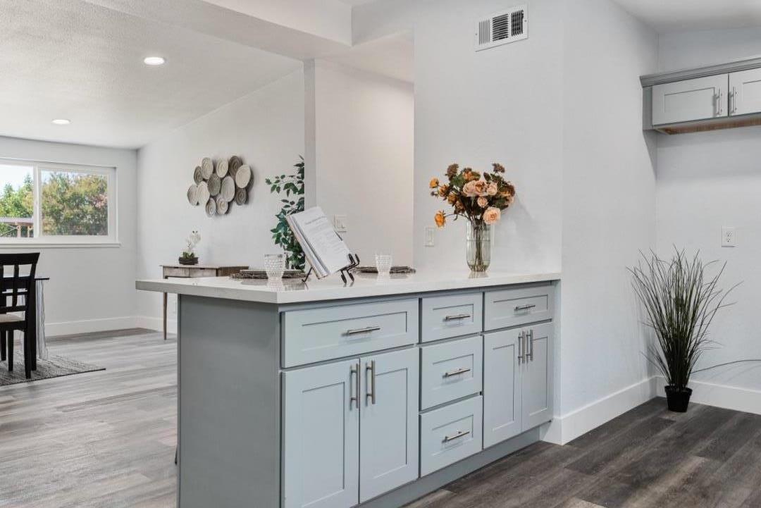Kitchen with a pale gray island, white countertop, and flowers beside a bright dining area.