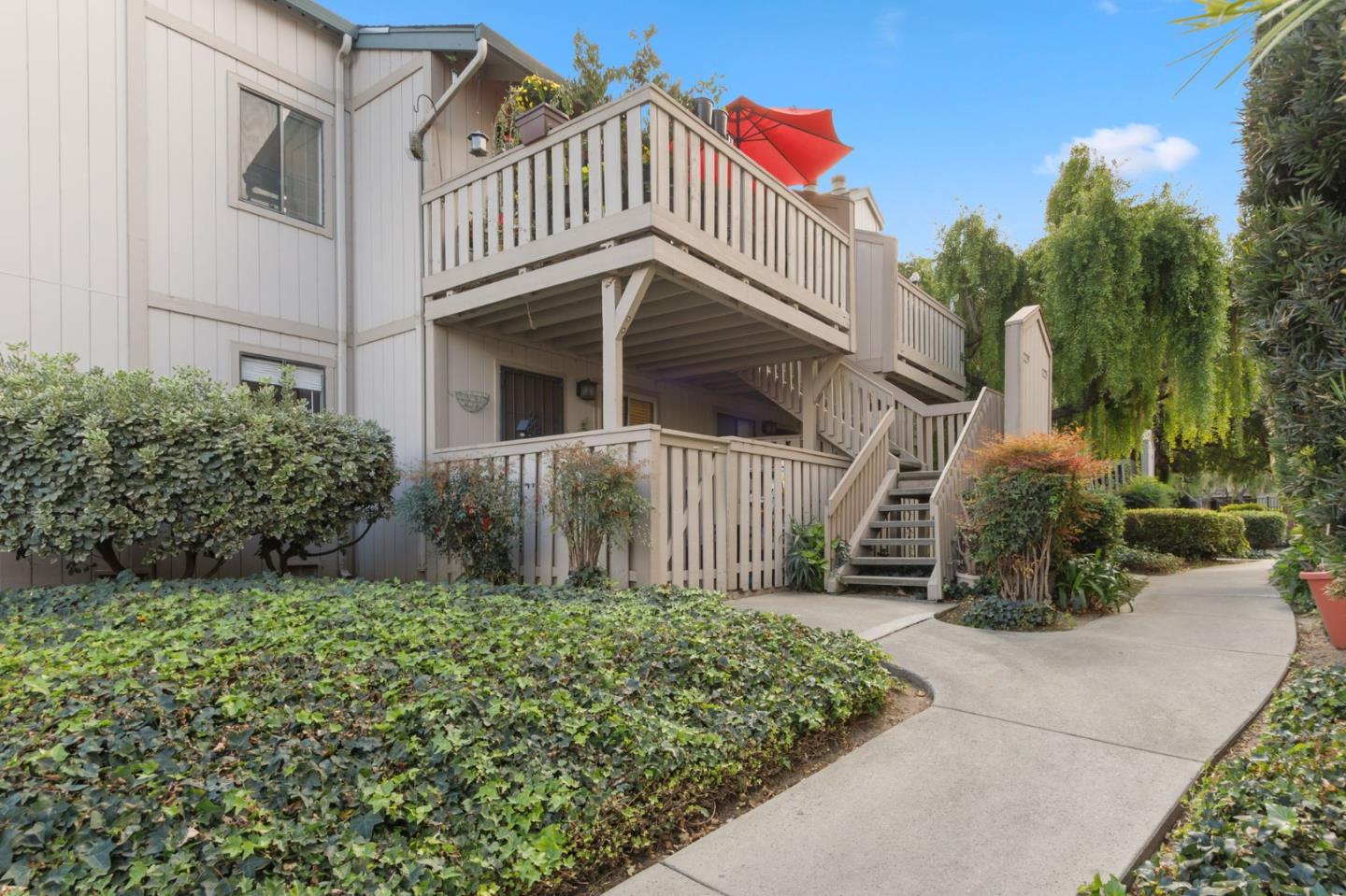 Residence with raised wooden decks, an exterior staircase, and a red patio umbrella amid landscaped grounds.