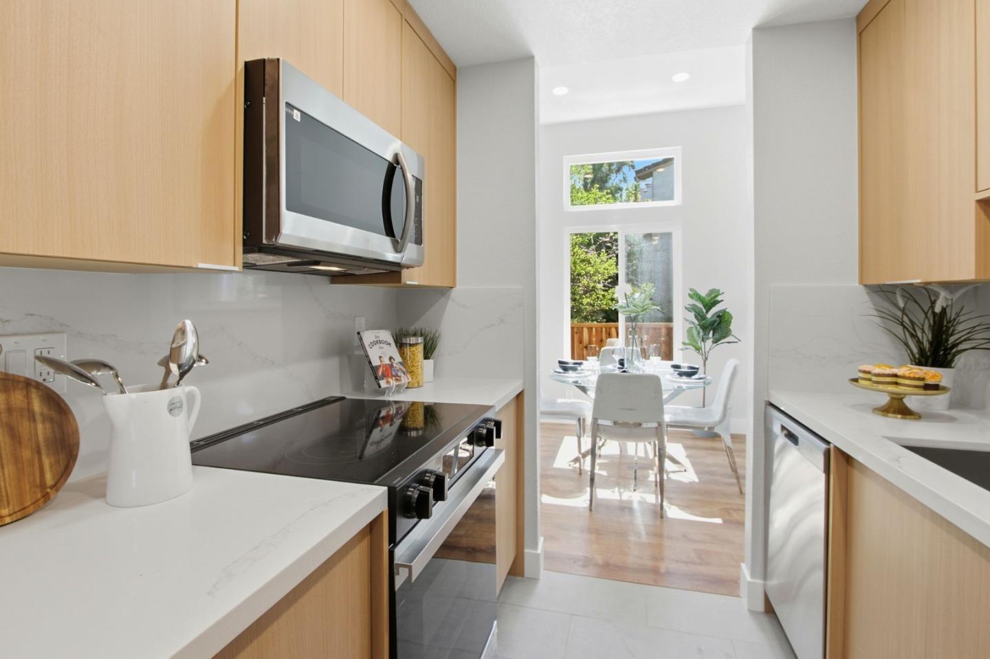 Modern kitchen with light wood cabinets and white counters opening to a sunny dining area.