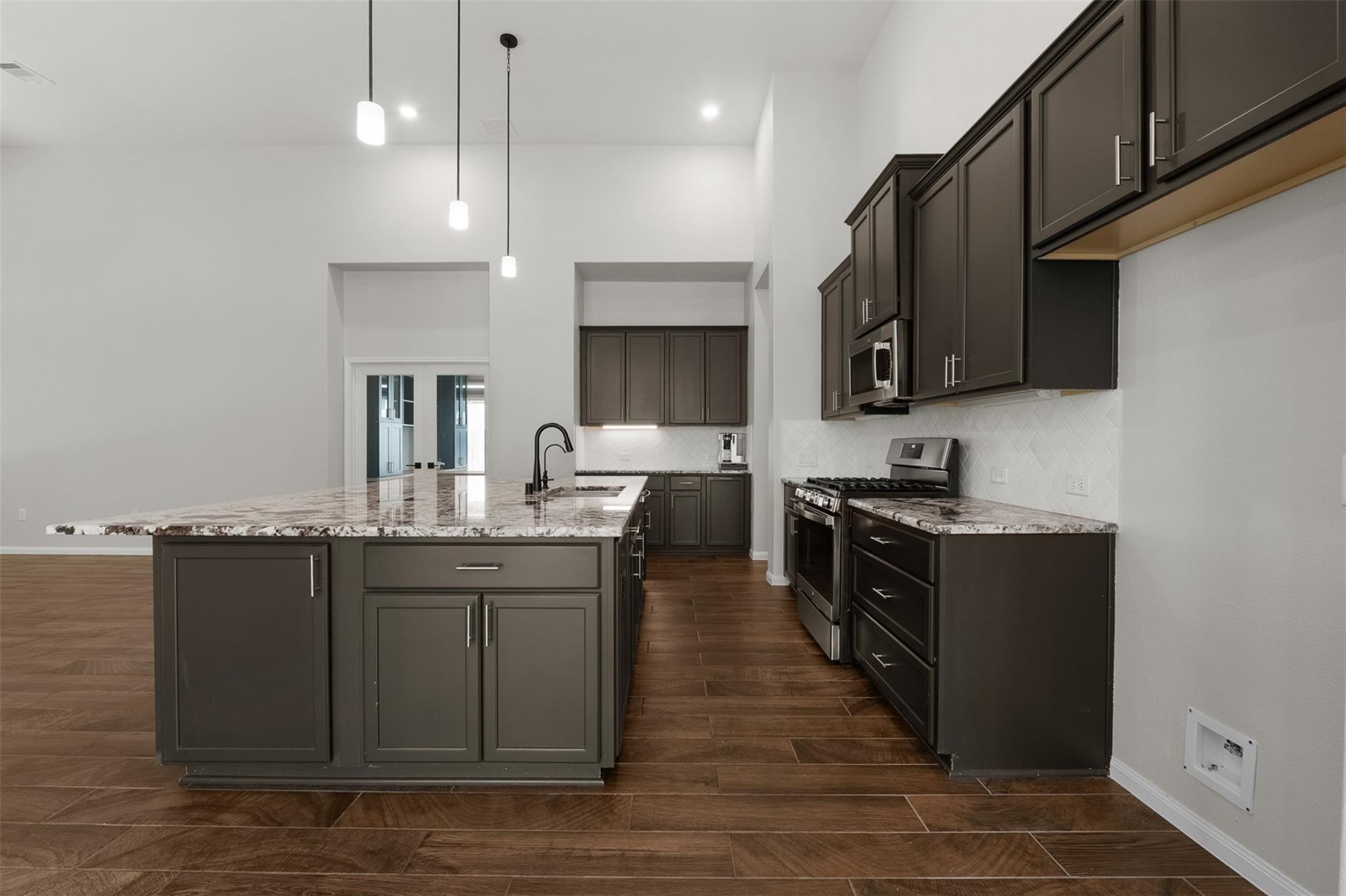 Vacant kitchen with dark cabinets, a large stone island, stainless steel appliances, and wood-look tile flooring.