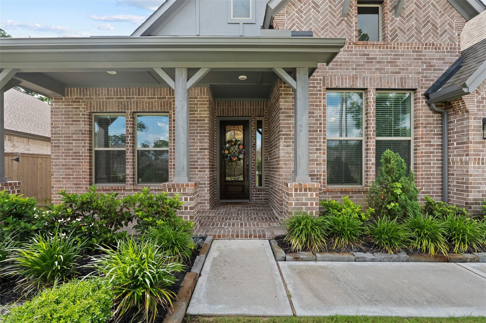 Two-story brick home with a covered entry, landscaped beds, and a walkway to the front door.