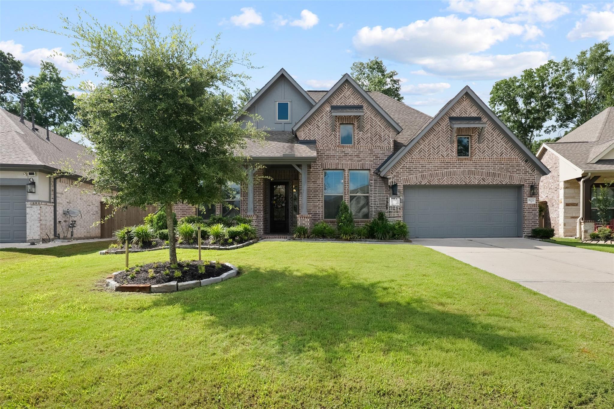 Two-story brick house with multiple gables, a gray double garage, and a landscaped front lawn.