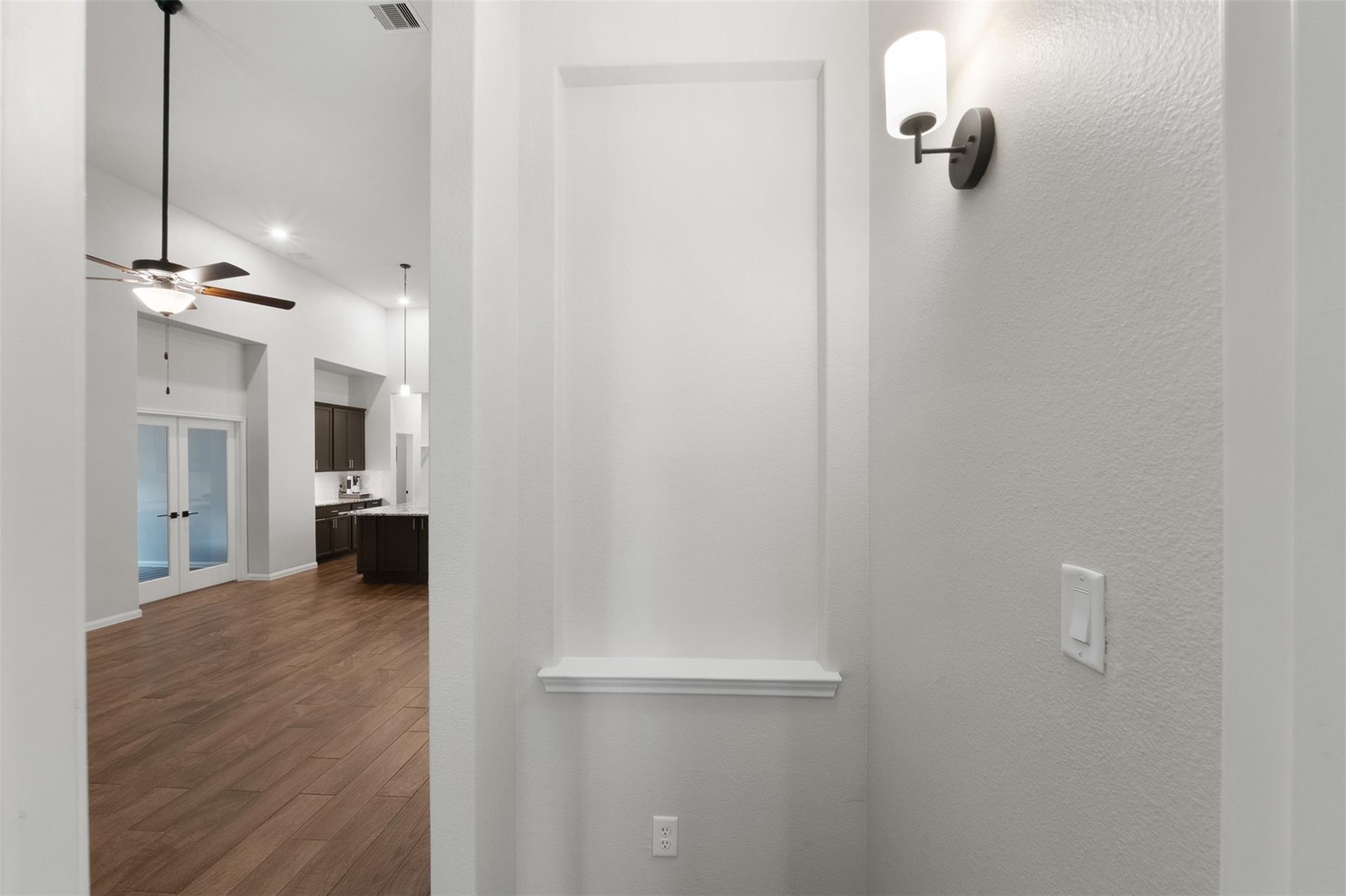 Recessed wall niche and sconce overlooking a wood-floored living area and kitchen.