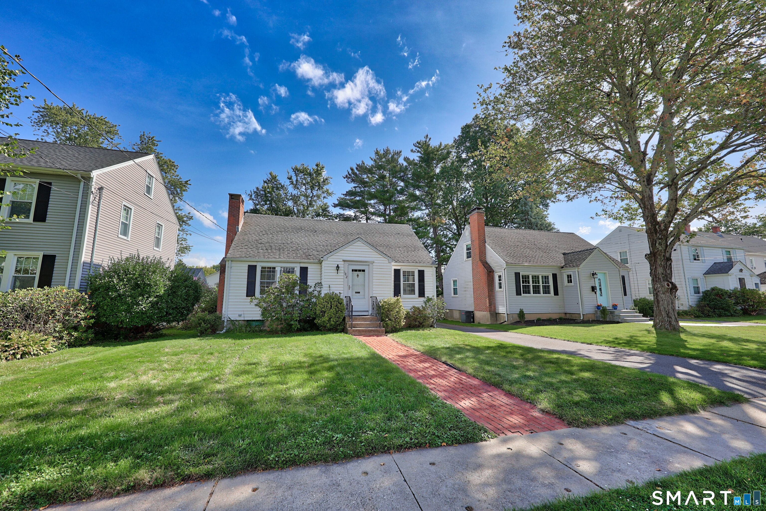 White single-story home with black shutters, a brick chimney, and a red brick front walkway.