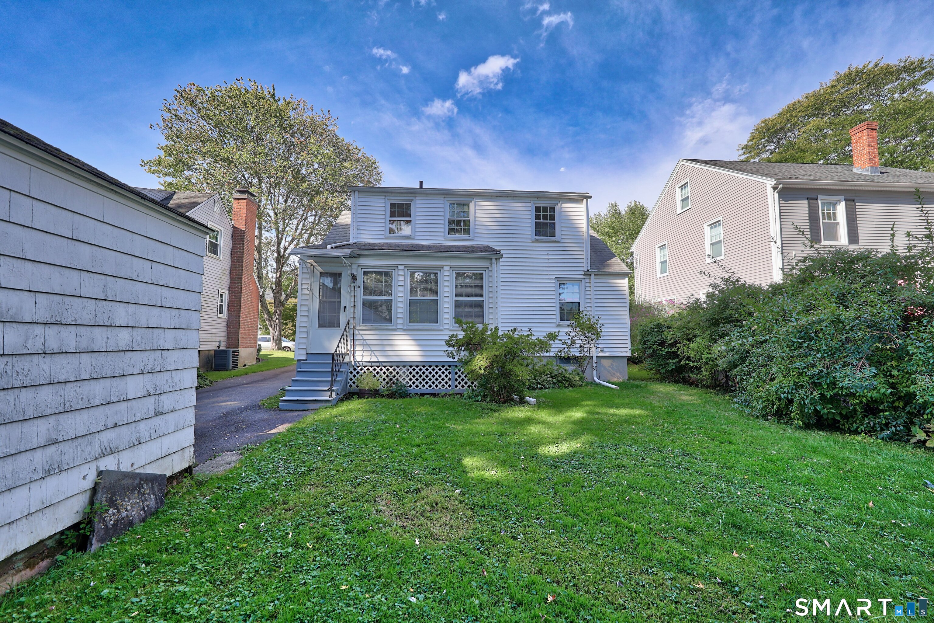 White two-story house viewed from the rear, with a raised entry, lattice skirting, and a broad green lawn.