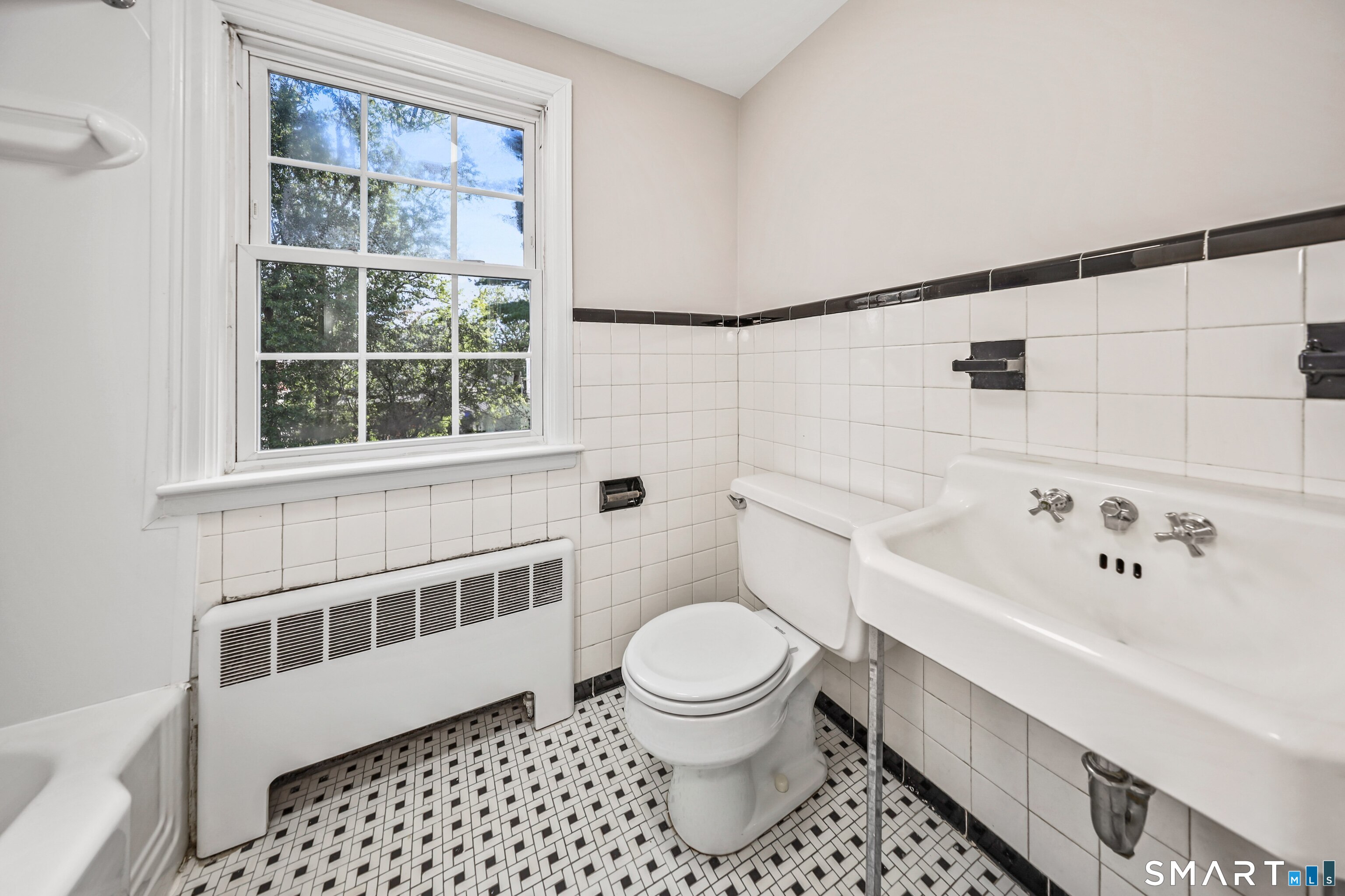 Bathroom with a pedestal sink, toilet, mosaic tile floor, and large window.