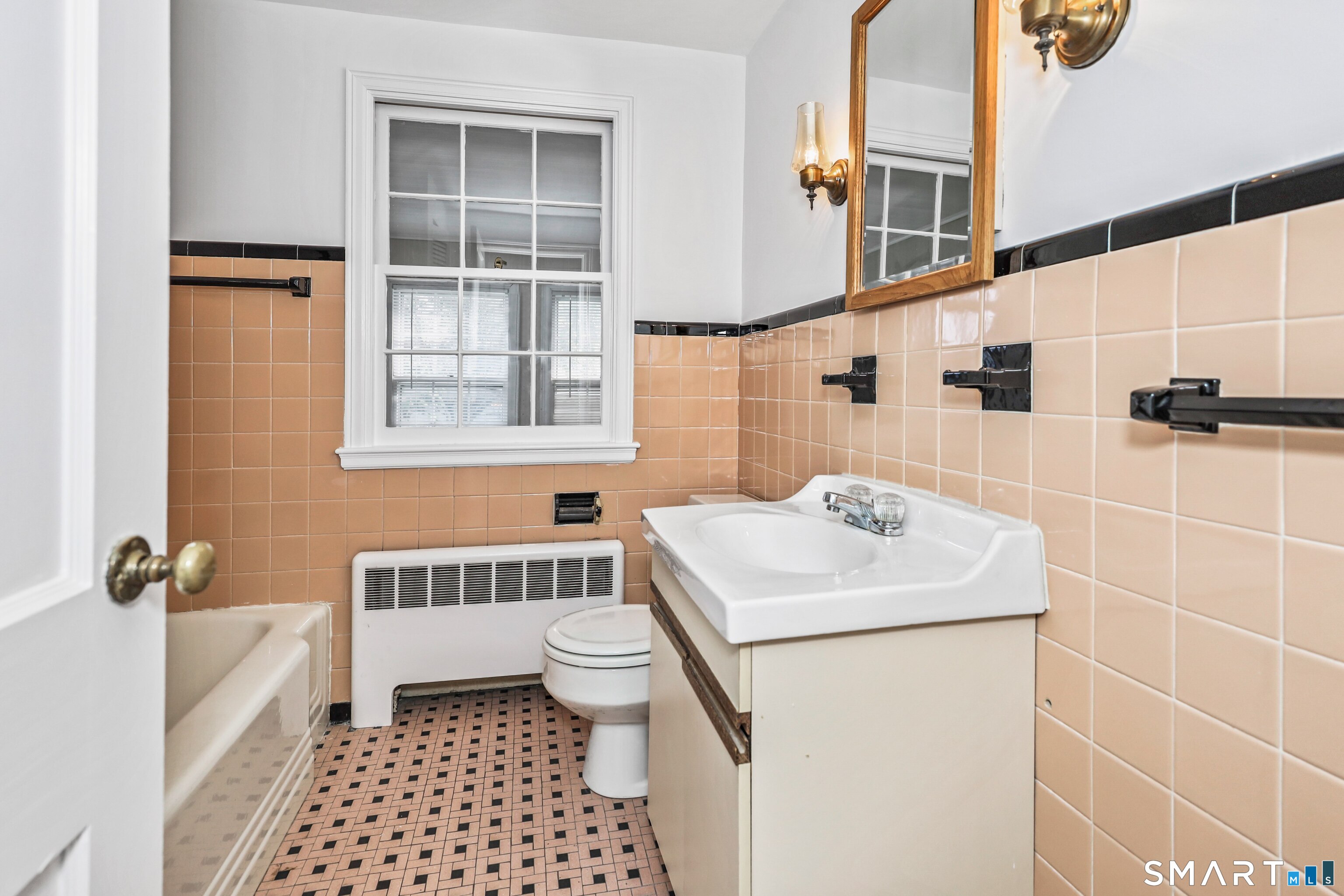 Bathroom with peach tile, mosaic flooring, a white tub, and a window above the toilet.